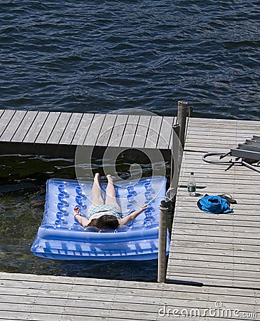 Teenage Girl Sunbathing On Raft At Lake